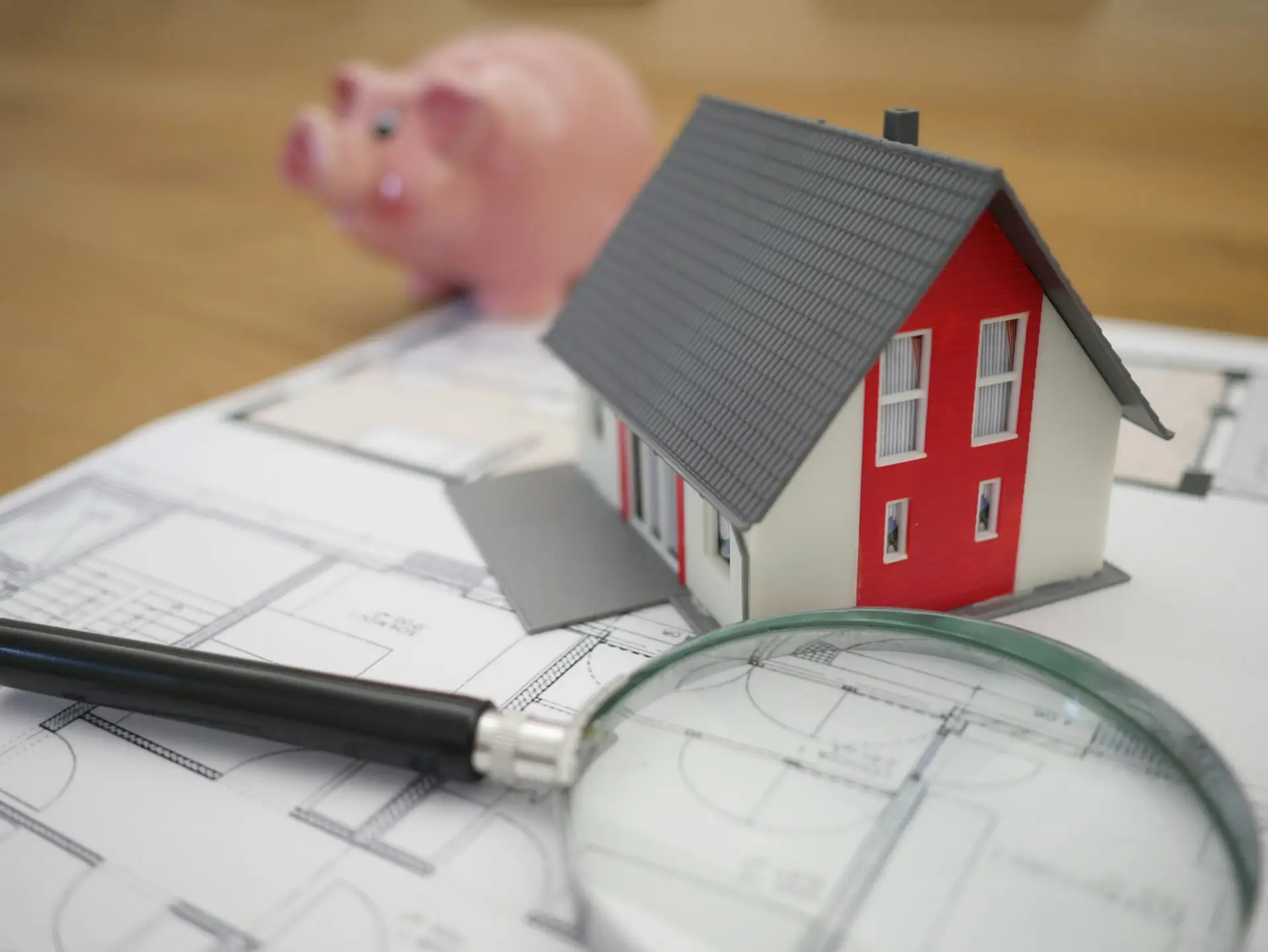 White and red wooden house next to a grey-framed magnifying glass, symbolizing home inspection or real estate.