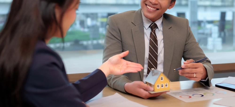 A property specialist discussing a housing loan Philippines Pag-IBIG vs Bank while holding a small house model.